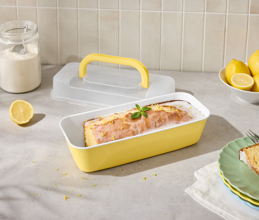 Zitronenkuchen in gelber Form mit Zitronen und Zuckerguss, angeschnitten auf Teller mit Gabel.