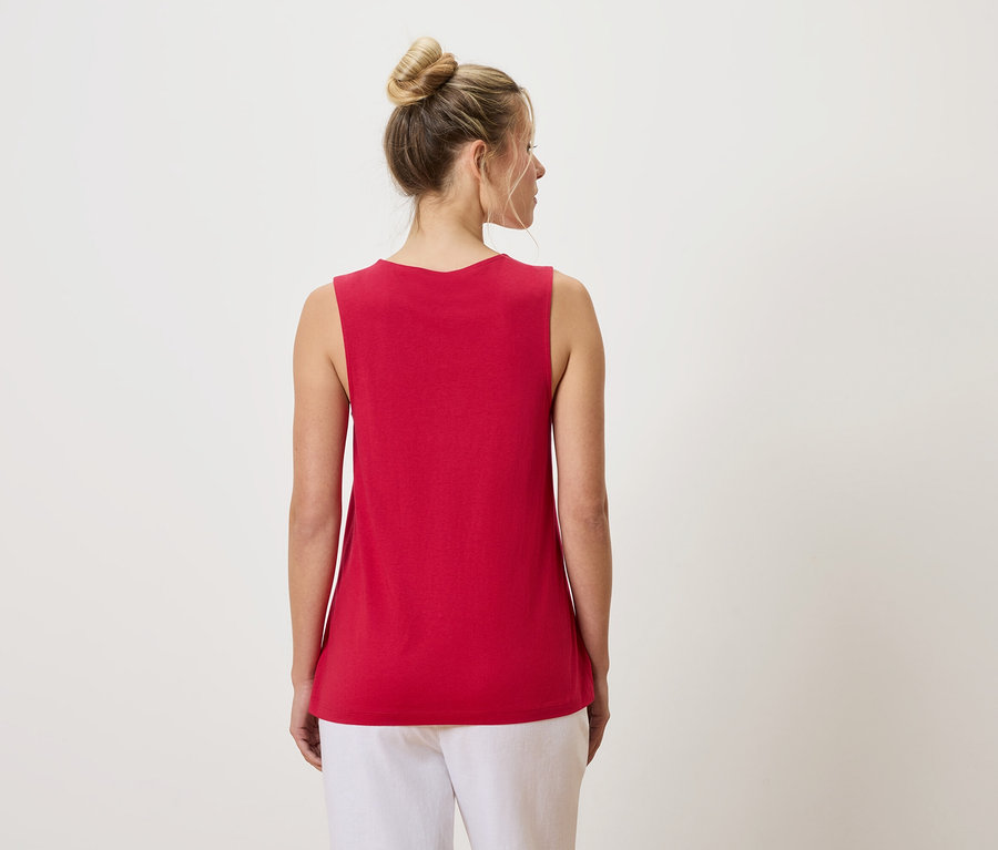 Rückansicht einer Frau mit Duttfrisur, die ein rotes Tanktop und weiße Hosen trägt.