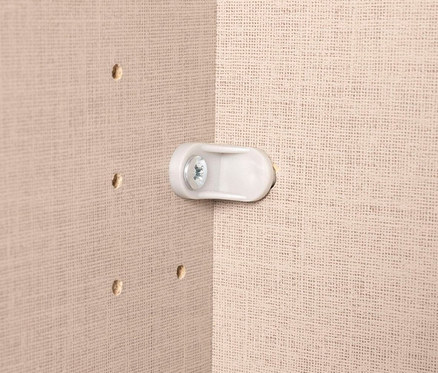 Nahaufnahme einer weißen Halterung mit Schraube an einer beigen Wand mit Löchern.