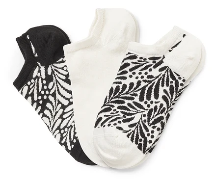 Drei Socken liegen nebeneinander, eine schwarz mit weißem Blattmuster, eine weiß und eine weiß mit schwarzem Blattmuster.