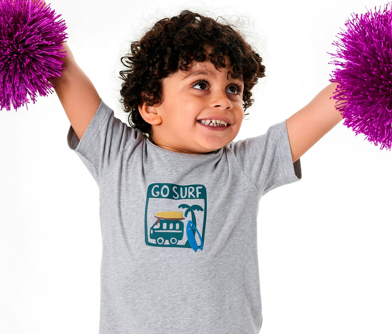 Junge mit lockigem Haar im SCHIESSER Kinder-Pyjama-Oberteil, hebt lila Pompons hoch.