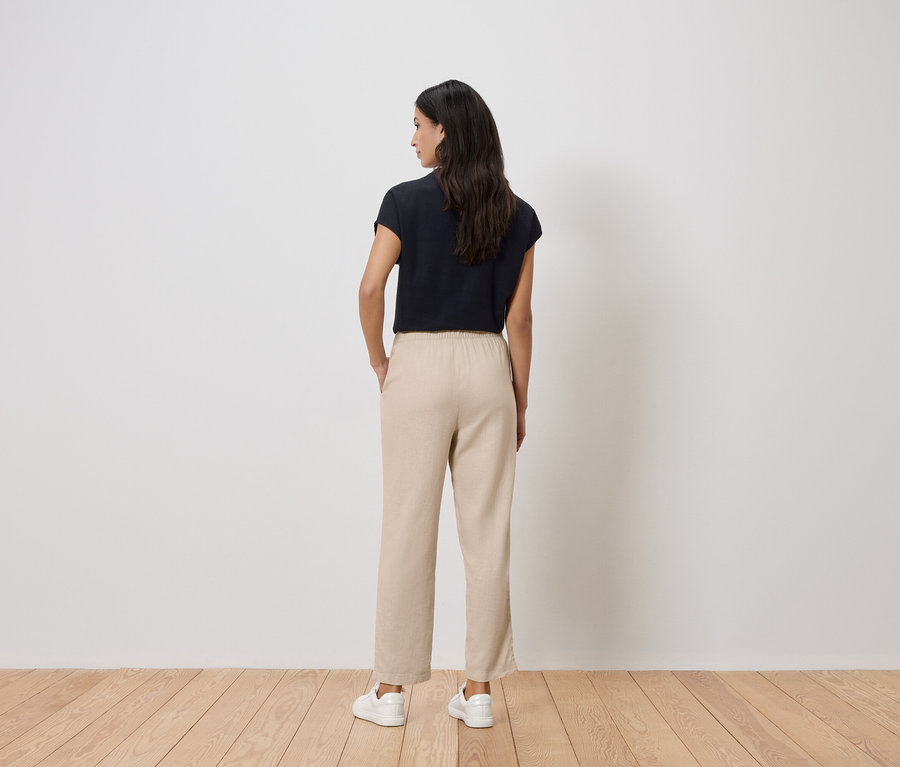 Rückansicht einer Frau mit dunklen Haaren, die ein schwarzes T-Shirt, eine beigefarbene Hose und weiße Turnschuhe trägt.