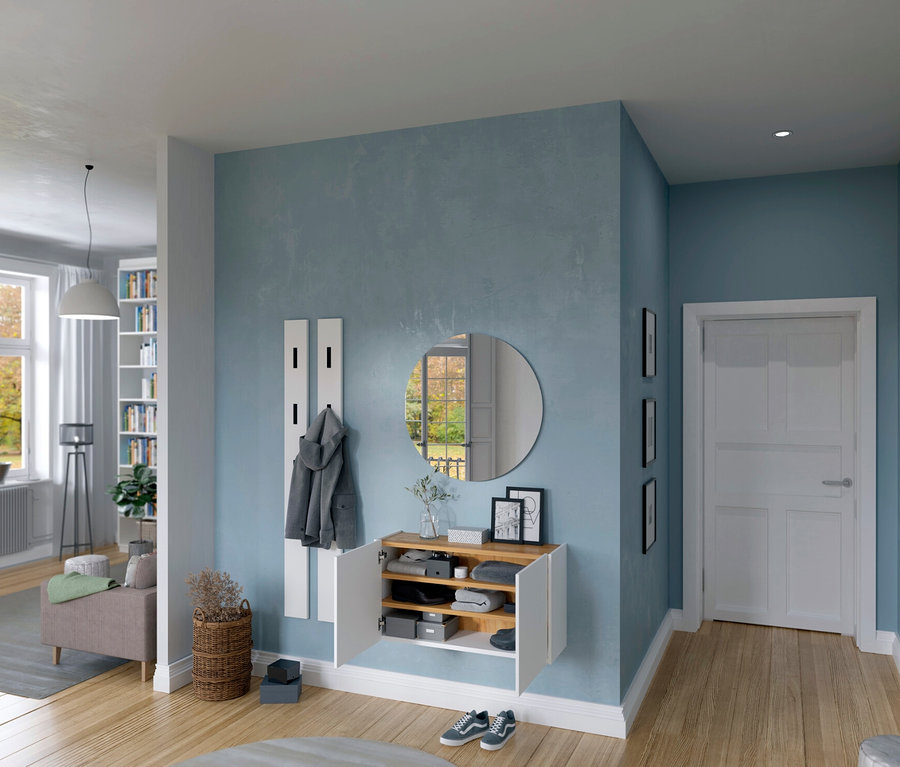 Flur mit Schuhschrank, Spiegel und Garderobe an blauer Wand. Durchgang zu Wohnzimmer mit Fenster und Couch.