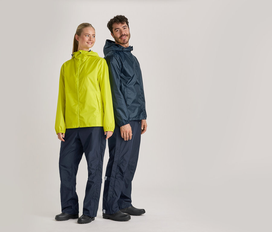 Eine Frau in gelber Regenjacke und ein Mann in marineblauer Regenjacke und Regenhose stehen vor einem grauen Hintergrund.