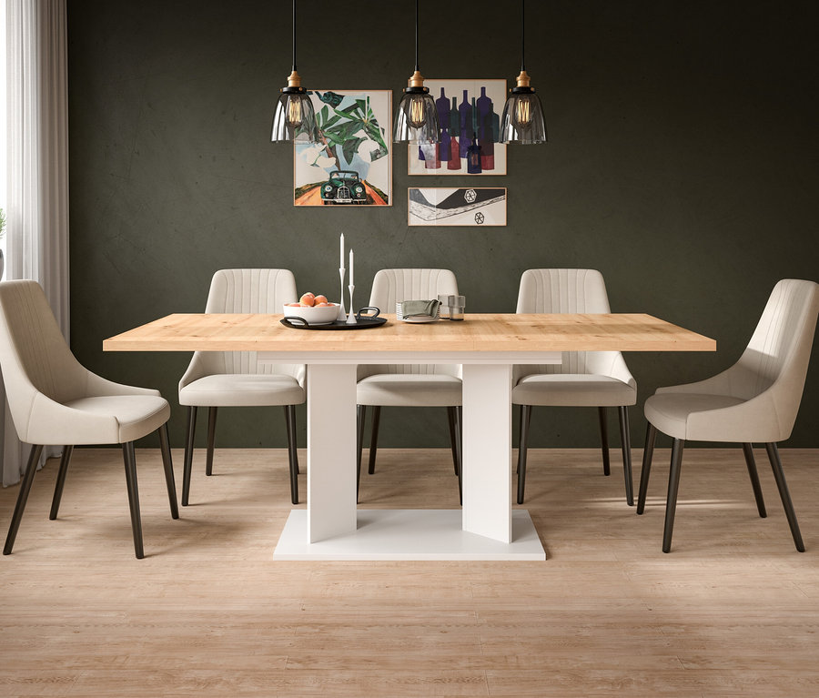 Ein Esszimmer mit einem rechteckigen Holztisch mit weißem Sockel, umgeben von sechs beigen Polsterstühlen. An der dunkelgrünen Wand hängen drei Bilder und drei Pendelleuchten. Auf dem Tisch stehen eine Schale mit Orangen und Kerzen.