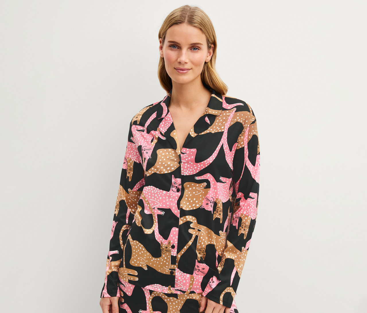 Blonde Frau lächelt und trägt ein schwarzes Langarmshirt mit einem Muster aus rosa und braun gefleckten Katzen.