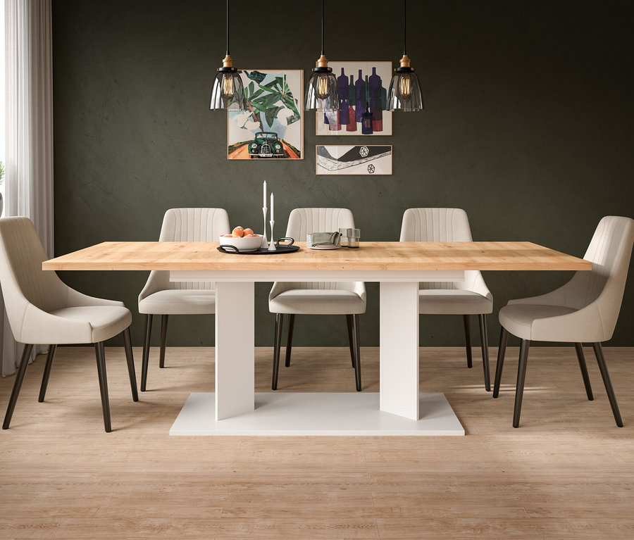 Modernes Esszimmer mit hellem Holztisch auf weißem Sockel, umgeben von sechs beigen Polsterstühlen. Über dem Tisch hängen drei Pendelleuchten, darauf stehen eine Obstschale, Kerzen und Geschirr. Dunkelgrüne Wände zeigen drei Kunstwerke, links ein Fenster mit Pflanze.