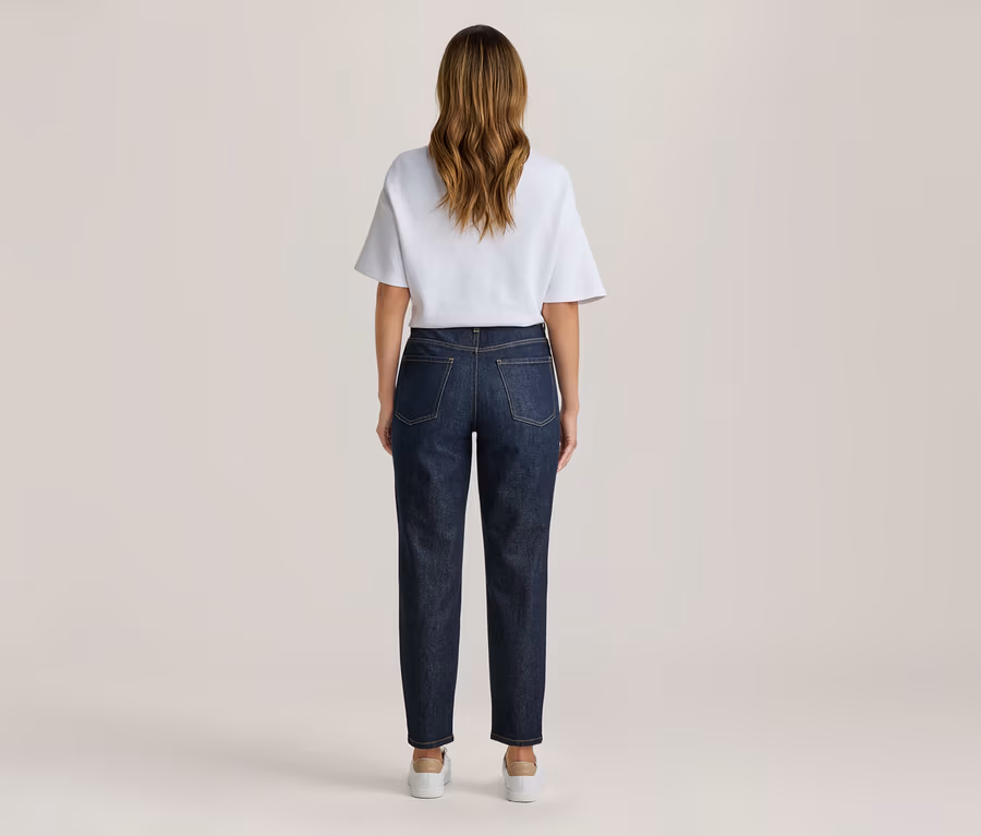 Frau von hinten stehend, trägt ein weißes T-Shirt und dunkelblaue Jeans mit hellen Sneakers.