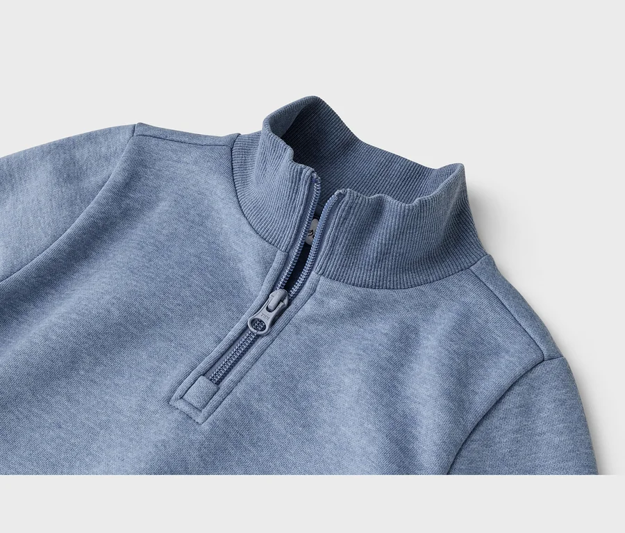 Nahaufnahme eines blauen Sweatshirts mit Stehkragen und Viertelreißverschluss, teilweise geöffnet.