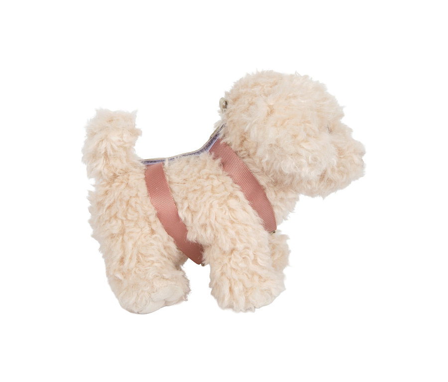 Cremefarbener flauschiger Plüschhund mit rosa Geschirr, von der Seite stehend.