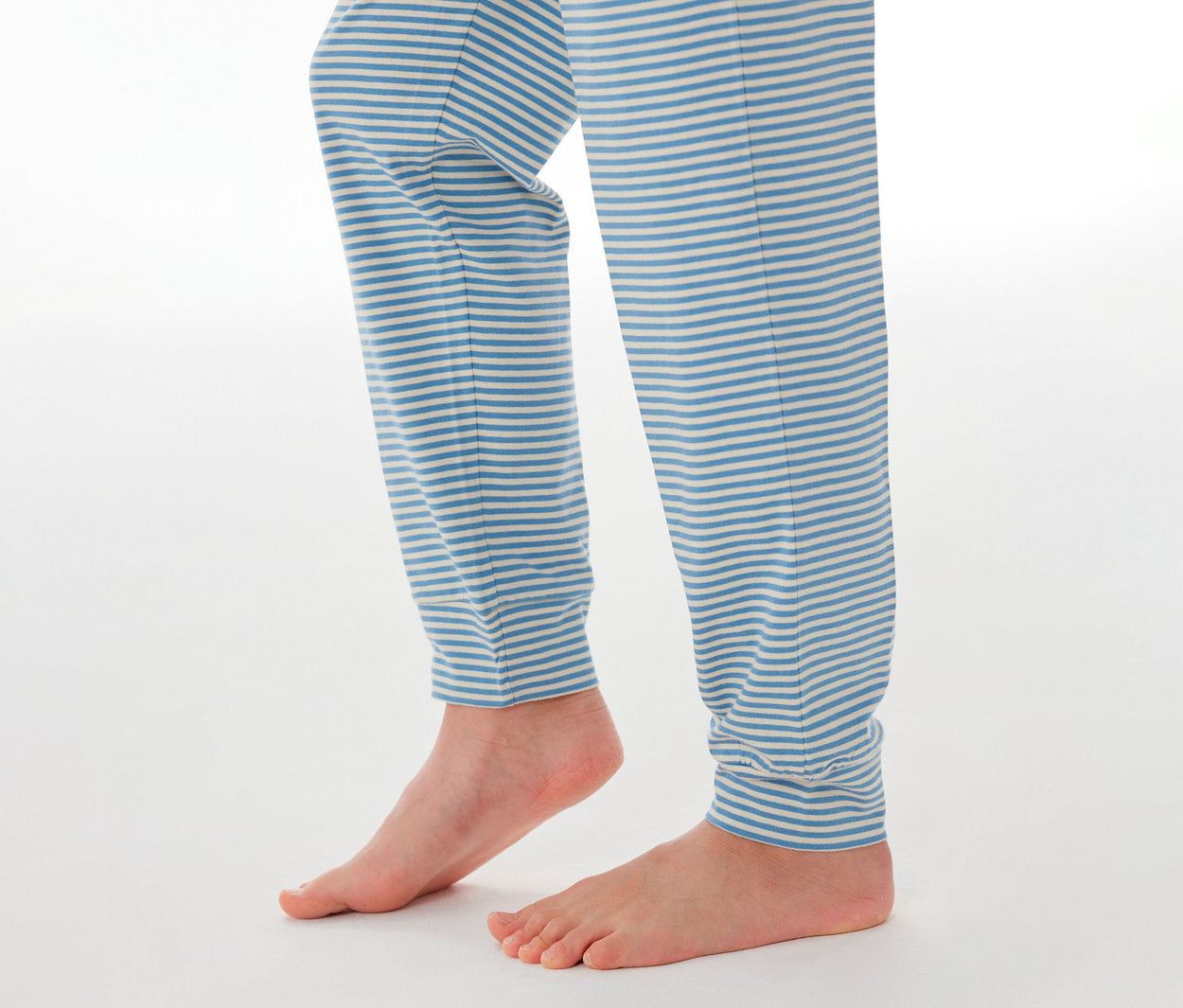 Kinderbeine und nackte Füße, die eine SCHIESSER Kinder-Pyjamahose mit blau-weißen Streifen tragen.