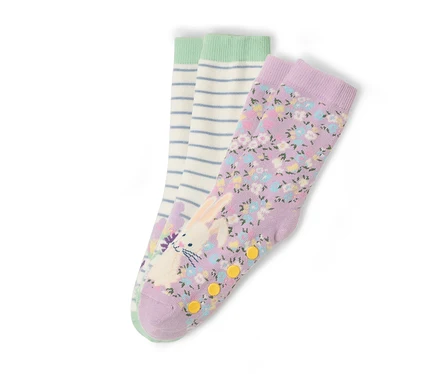 Drei Sockenpaare liegen auf einem weißen Hintergrund. Ein Paar ist lila mit einem Blumenmuster und einem Hasenaufdruck. Ein Paar ist weiß mit blauen Streifen und einem grünen Bund.