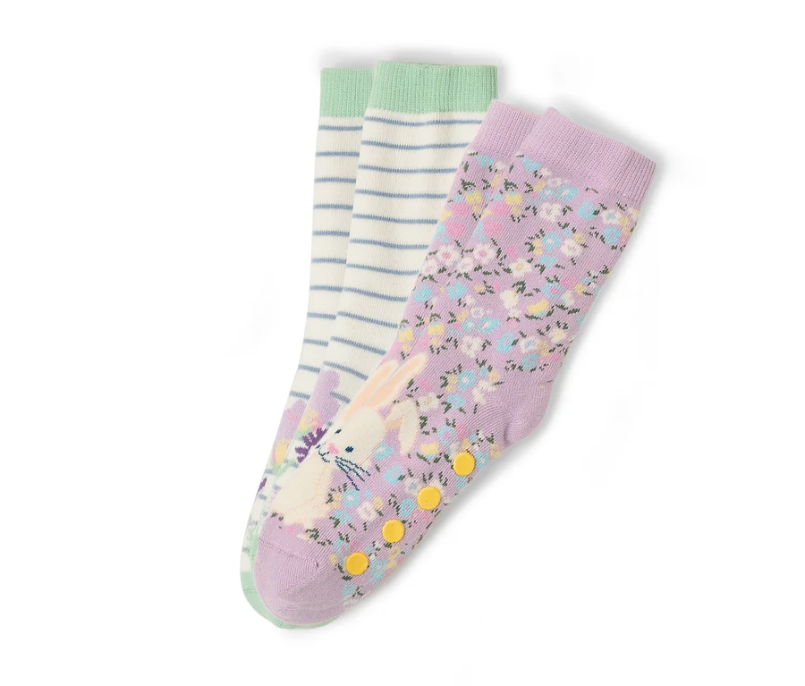 Drei Sockenpaare liegen auf einem weißen Hintergrund. Ein Paar ist lila mit einem Blumenmuster und einem Hasenaufdruck. Ein Paar ist weiß mit blauen Streifen und einem grünen Bund.