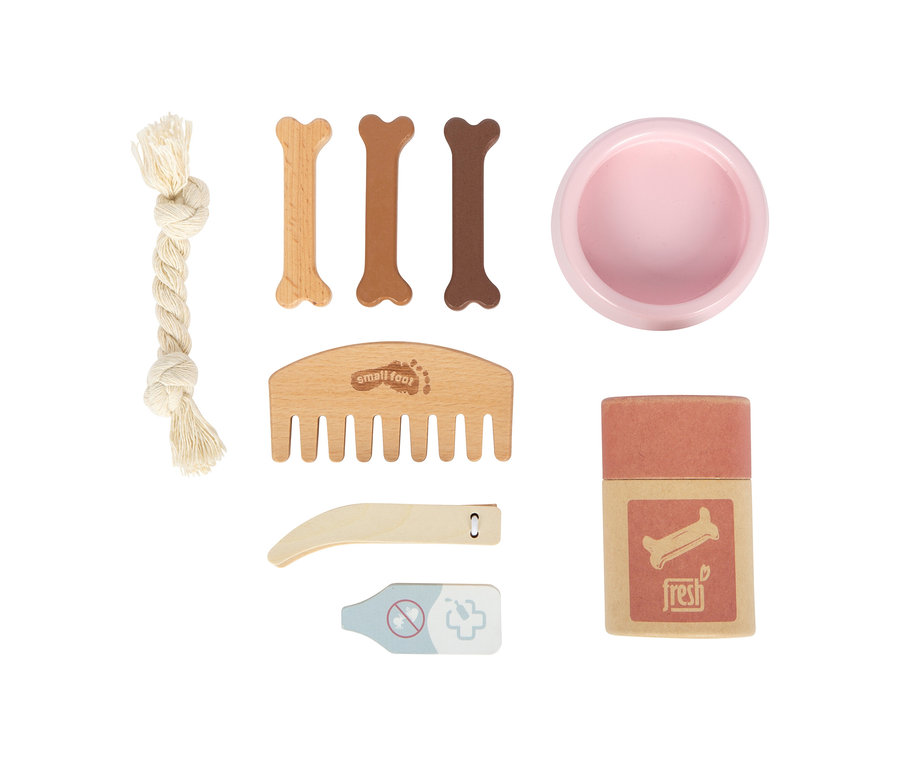 Ein small foot Pflege-Set für Haustiere, bestehend aus einem weißen Seilspielzeug, drei knochenförmigen Holzleckerlis, einer rosa Schale, einem Holzkamm, einer Holzkrallenschere, einem Holzthermometer und einer Box mit der Aufschrift „fresh“ und einem Knochensymbol.
