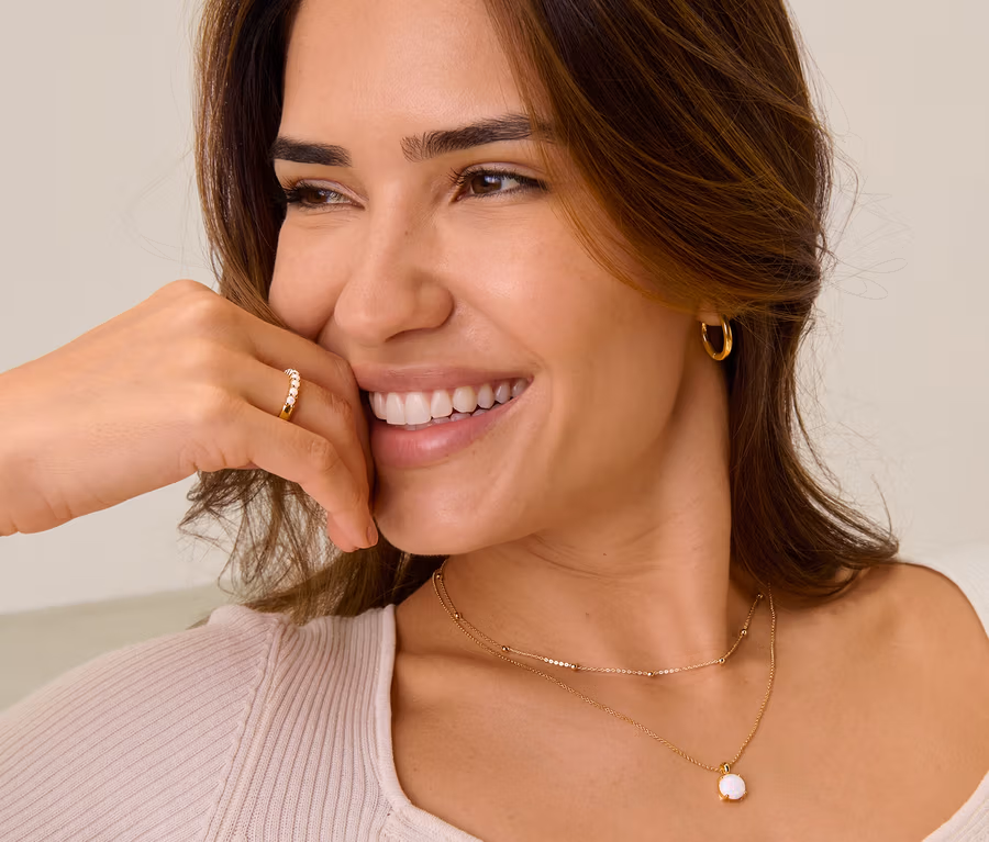 Lächelnde Frau mit goldfarbenem Creolen-Set, einem 925 Silber Ring mit synthetischen Opalen, einer 925 Silber Kette mit synthetischem Opal und einer 375 Gold Kette Kugeln.