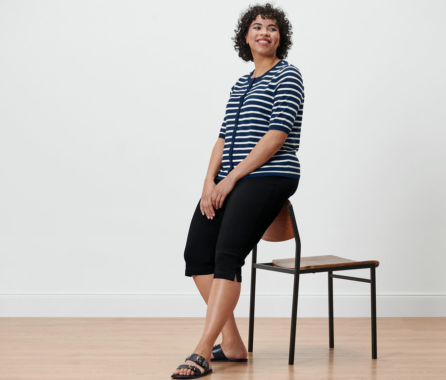 Frau sitzt auf einem Stuhl und trägt eine 3/4-Bengalin-Hose, schwarz.