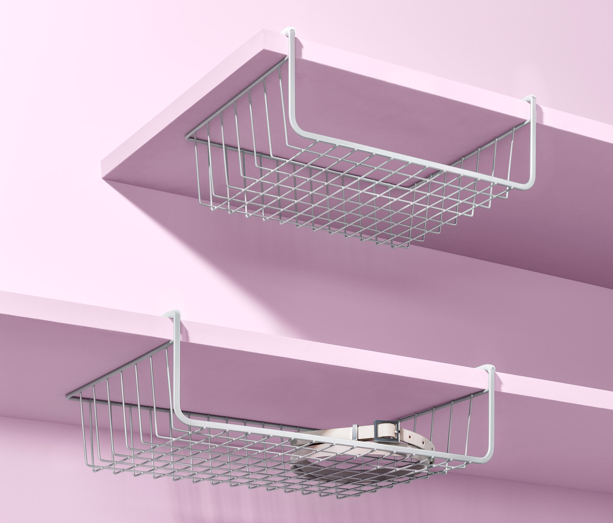 Zwei Schrankkörbe zum Einhängen hängen unter Regalen vor einem rosa Hintergrund.