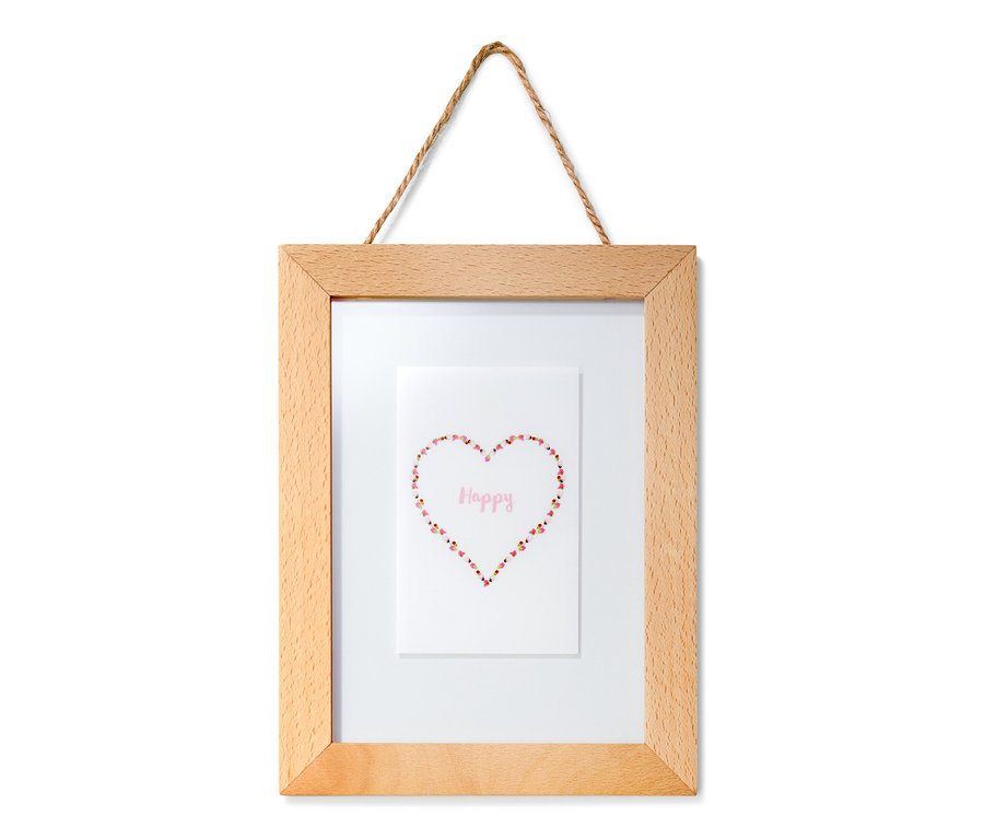 Ein hölzerner Bilderrahmen mit einem Bild eines Herzens aus Blumen und dem Wort Glücklich, an einer Wand hängend.