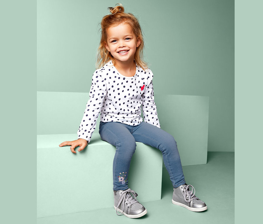 Mädchen sitzt und trägt ein gepunktetes Oberteil und Treggings.