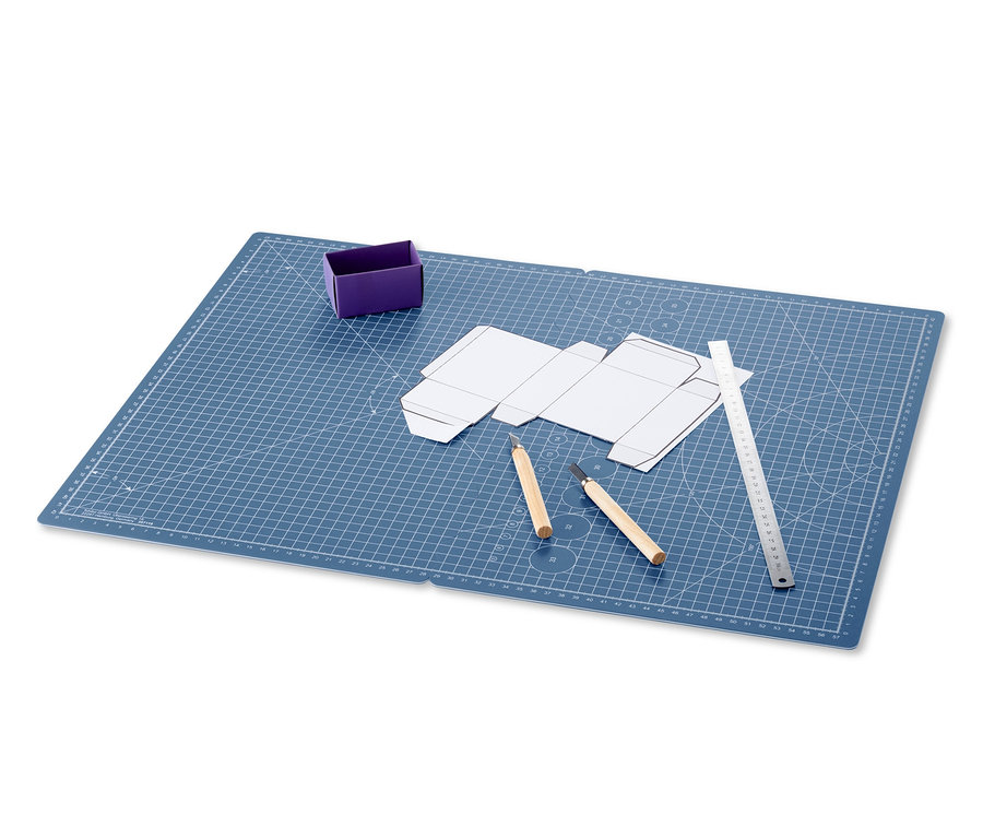 Eine blaue faltbare Schneide- und Bastelunterlage mit einem Papiermodell, Messern und einem Lineal.