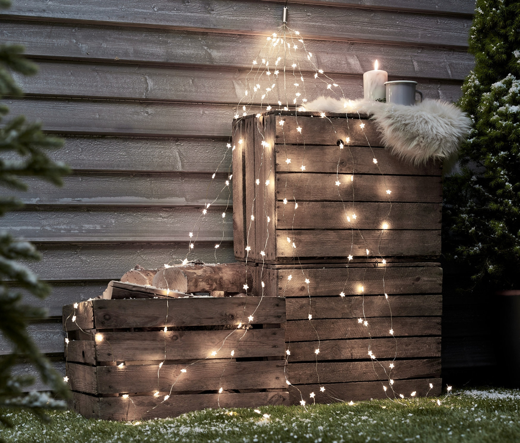Holzkisten sind gestapelt und mit LED-Lichtschweifen, einer Kerze, Fell und einer Tasse dekoriert.