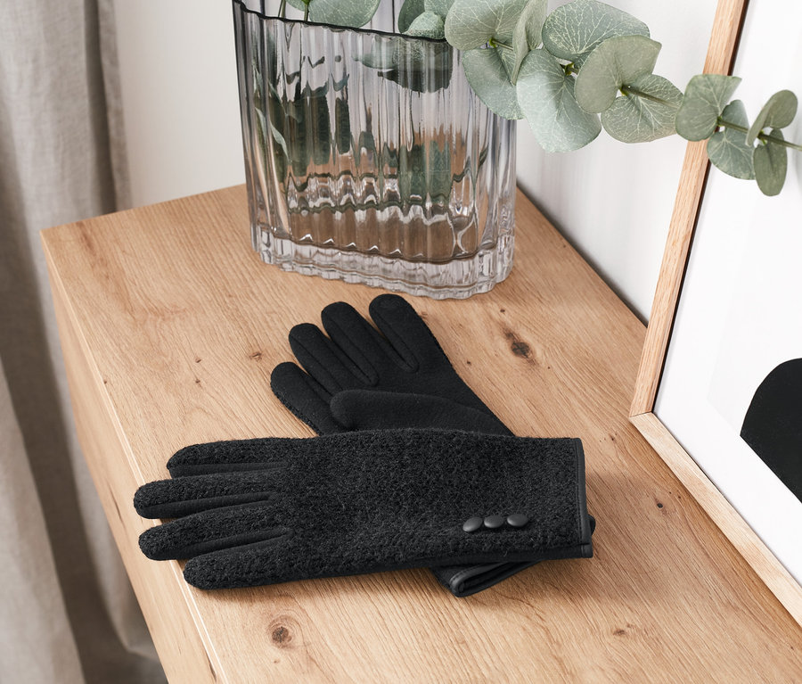 Auf einer Holzkommode liegen schwarze Handschuhe im Materialmix.