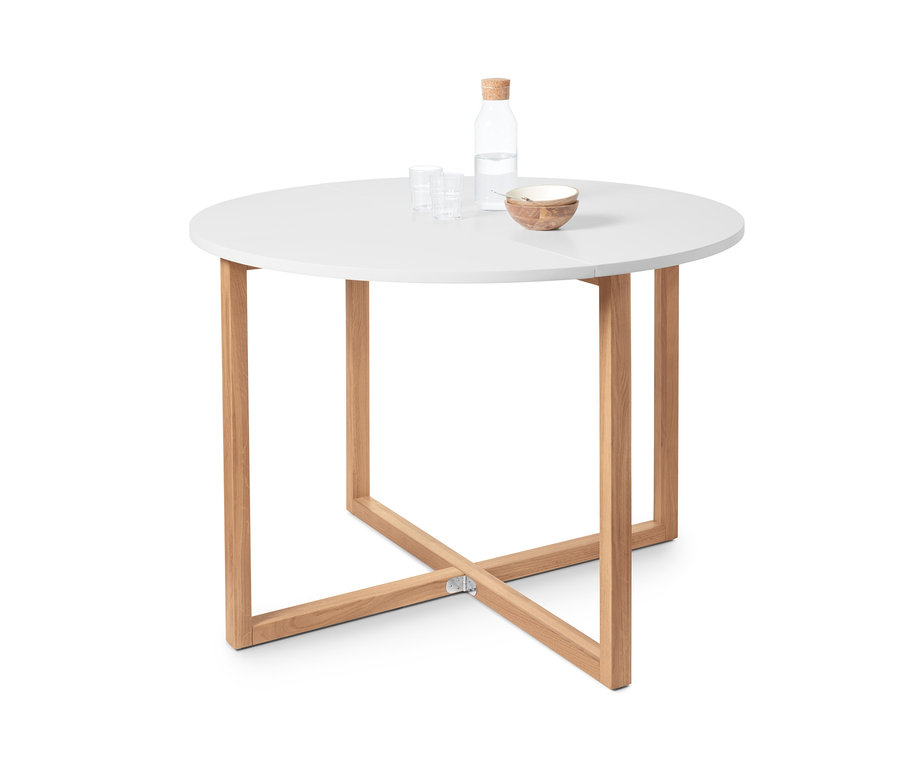 Ein klappbarer Esstisch mit einer runden, weißen Tischplatte und Holzbeinen. Auf dem Tisch stehen eine Wasserflasche, zwei Gläser und eine Schale.