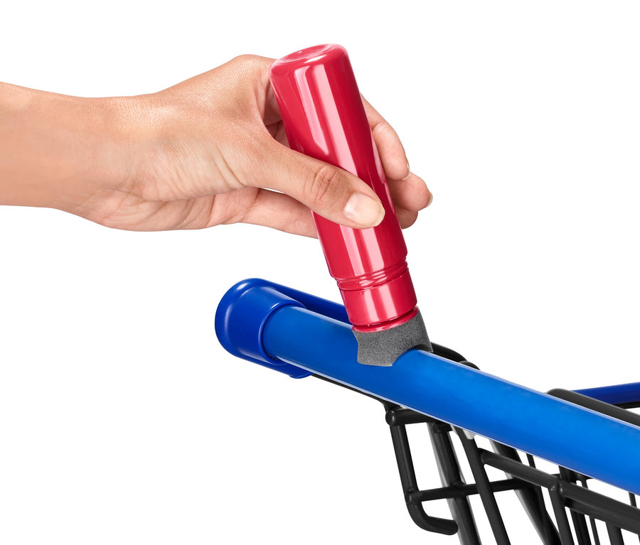 Eine Hand trägt einen Desinfektionsstift auf den blauen Griff eines Einkaufswagens auf.