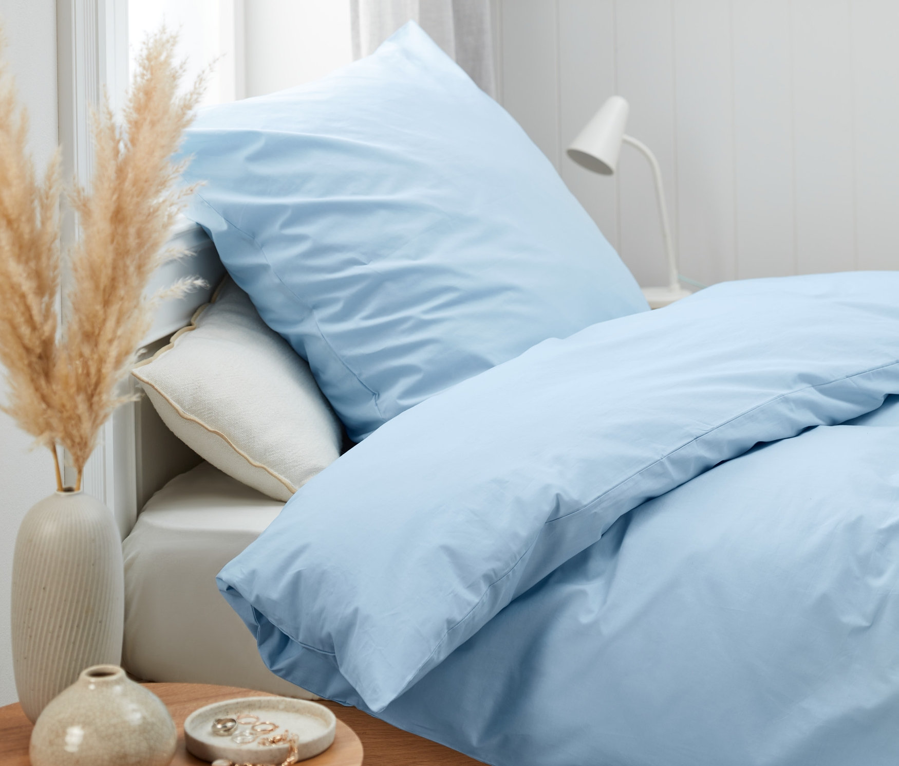 Blaue Perkal-Bettwäsche in Normalgröße und Übergröße auf einem Bett.