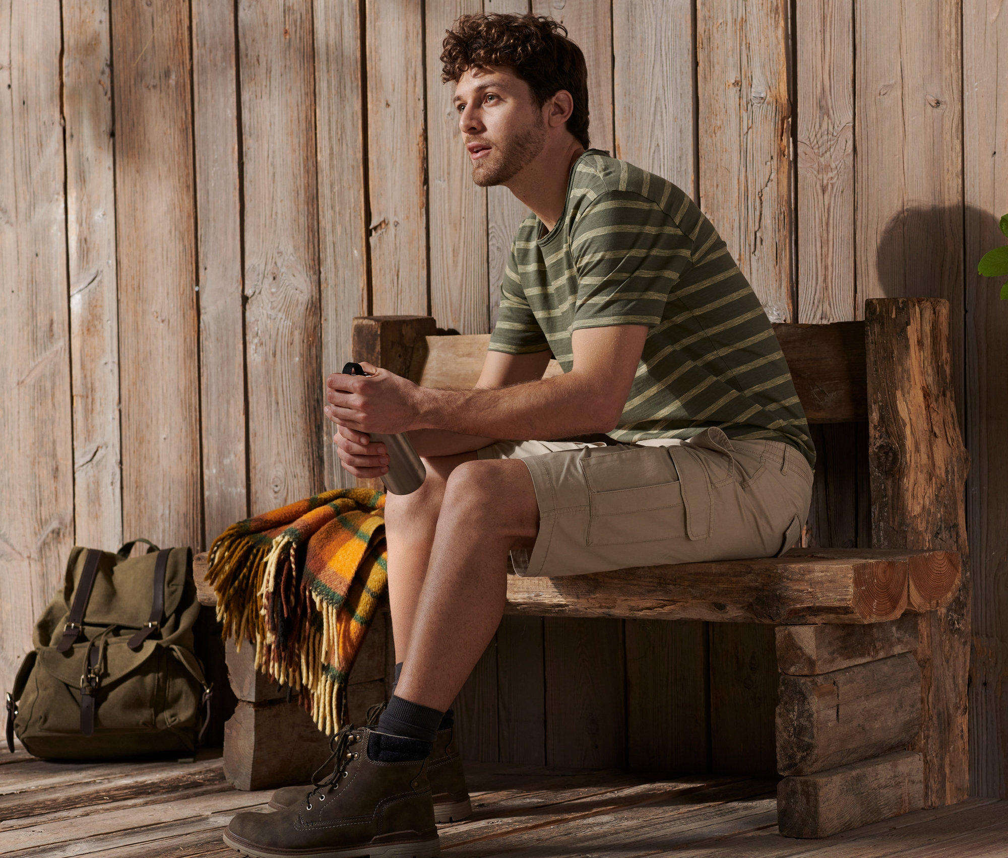 Mann sitzt auf Holzbank mit Trinkflasche, trägt sandfarbene Cargo-Bermuda.