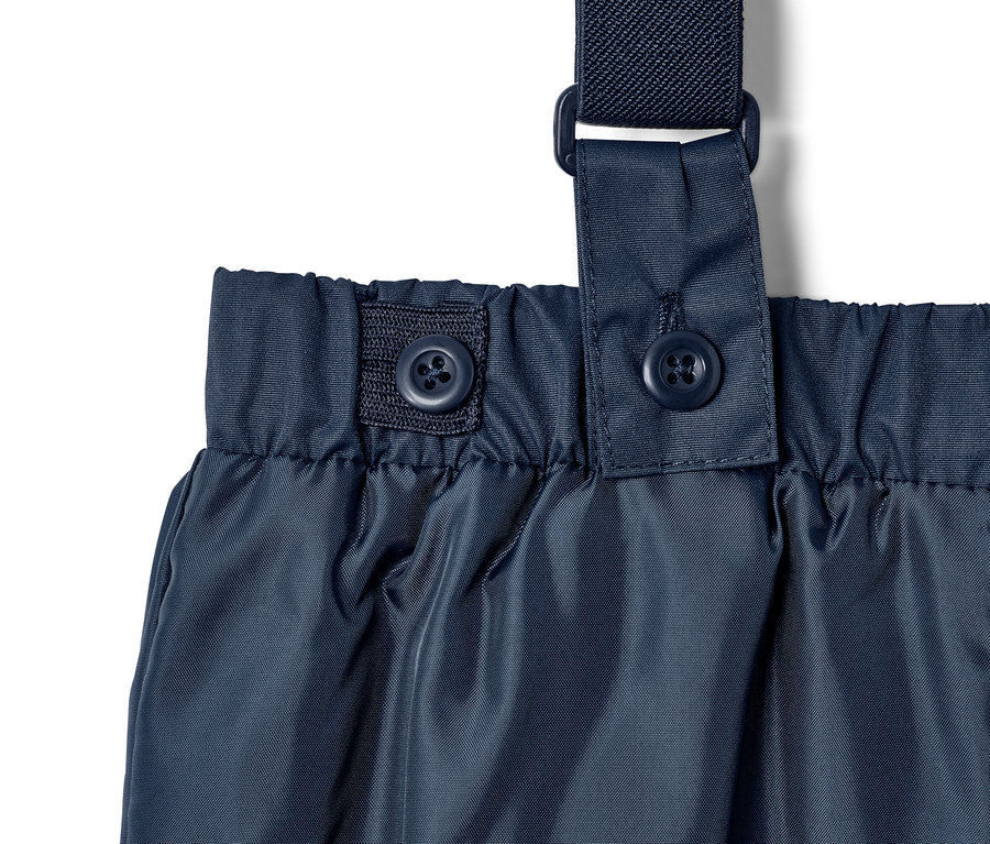 Detailaufnahme einer blauen Regenhose mit Trägern und Knöpfen.
