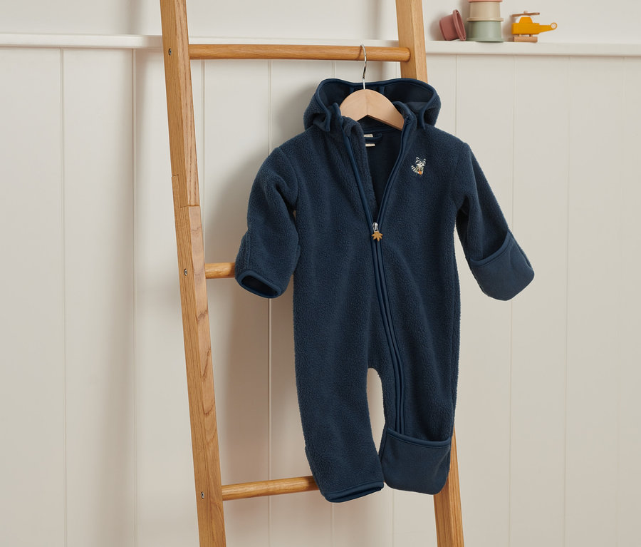 Ein marineblauer Fleece-Einteiler hängt an einer Holzleiter.