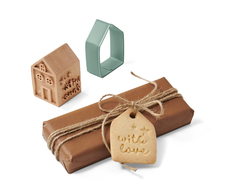 Ein braunes, verpacktes Geschenk mit einem 'With Love'-Tag, ein hölzernes und ein grünes Keksstempel-Set in Hausform.