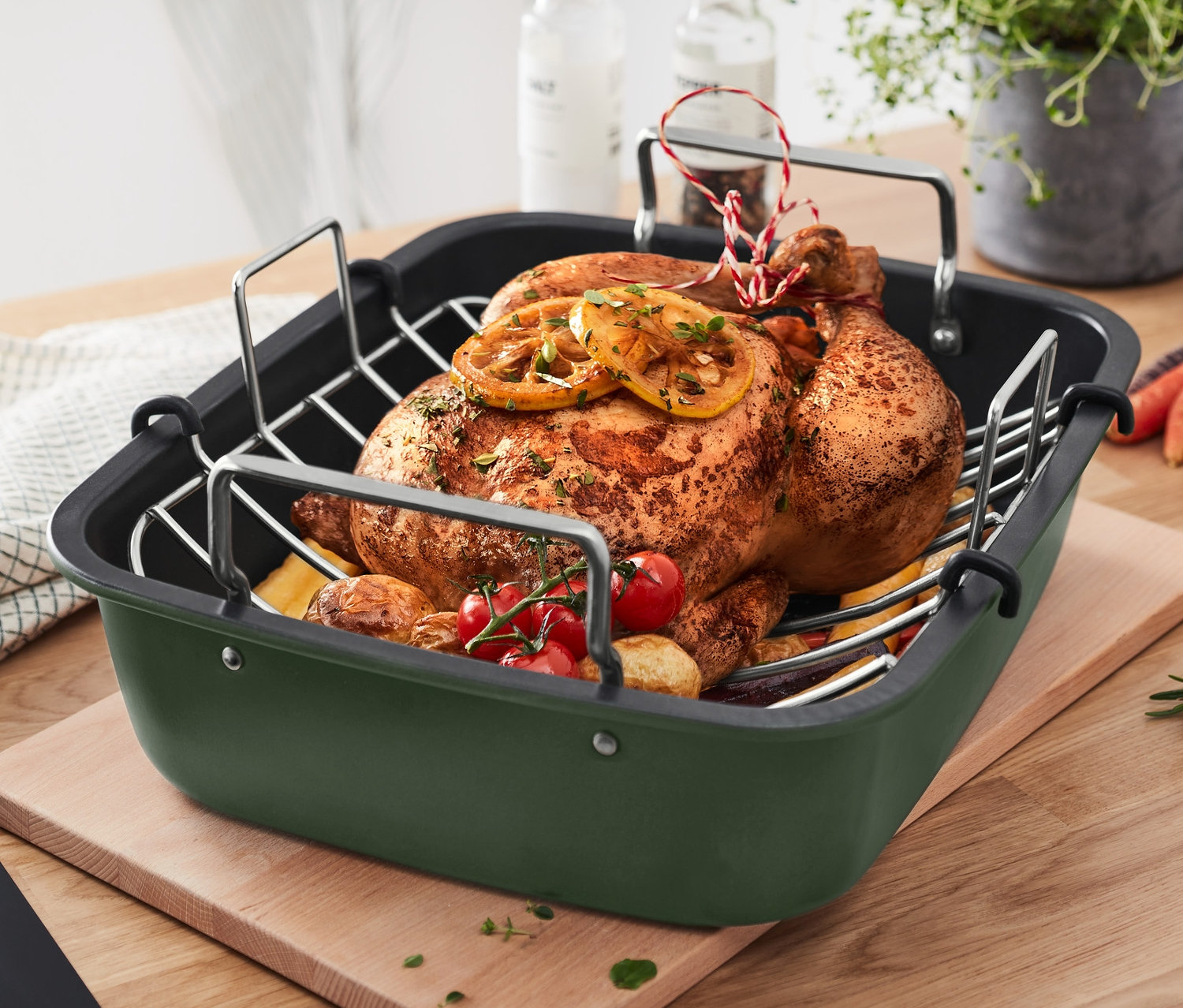 Gebratenes Hähnchen mit Zitrone und Gemüse in einem XL-Edelstahl-Bräter mit Rost auf einem Holzbrett.