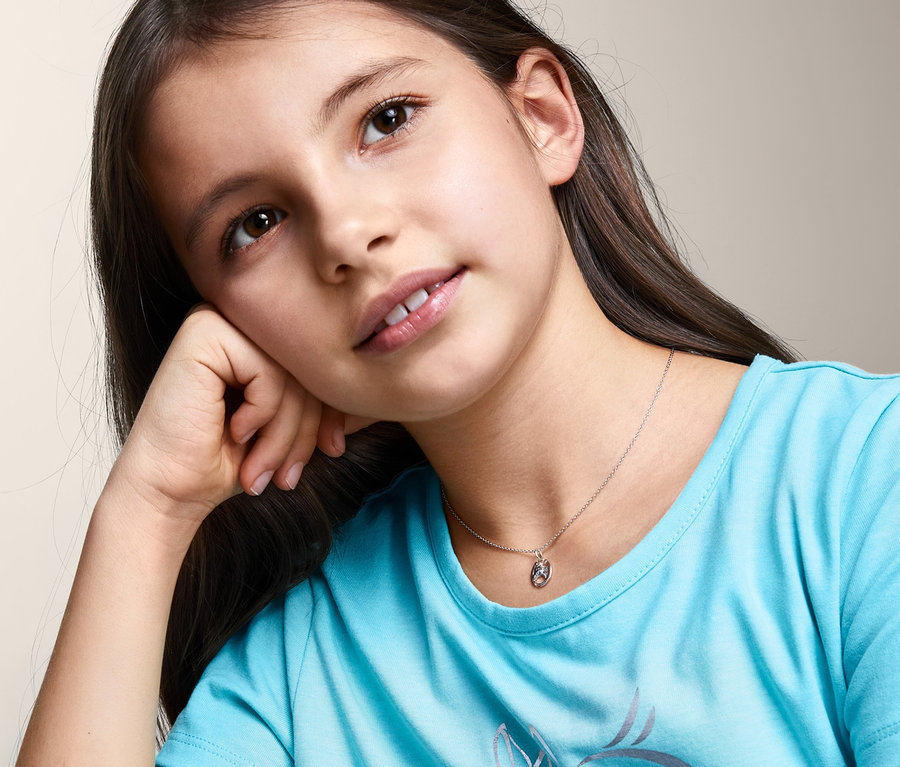 Porträt eines jungen Mädchens mit braunen Haaren, das ein blaues T-Shirt mit Pferdeaufdruck und eine silberne Kette, 925 Silber, mit Pferdeanhänger trägt.