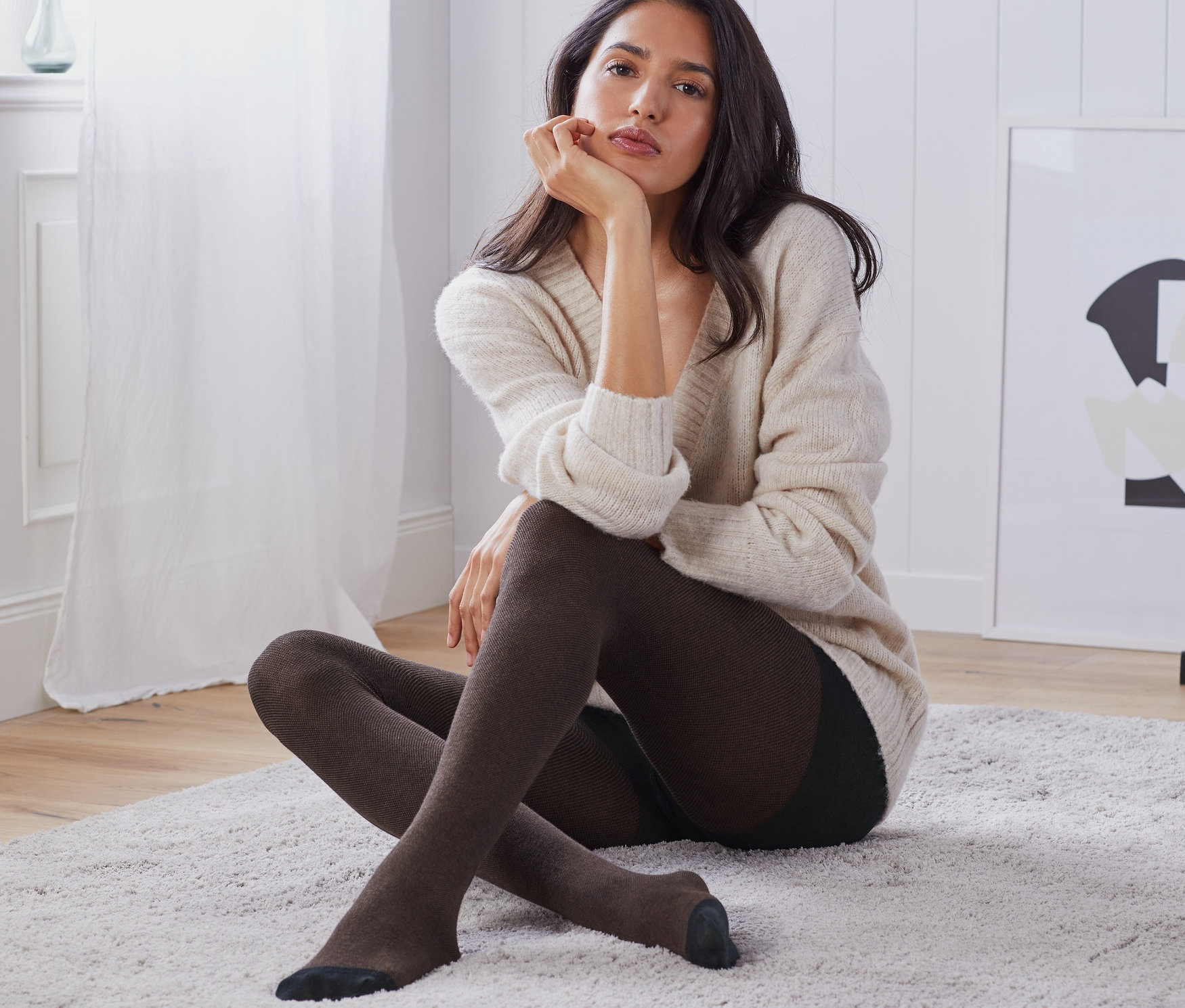 Eine Frau sitzt auf einem Teppich und trägt eine Struktur-Strumpfhose.