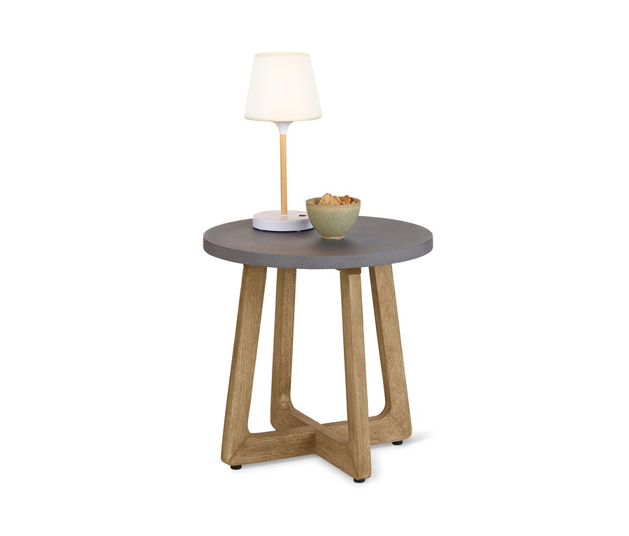 Auf einem runden Beistelltisch mit Beton-Tischplatte stehen eine Lampe und eine Schale mit Essen.