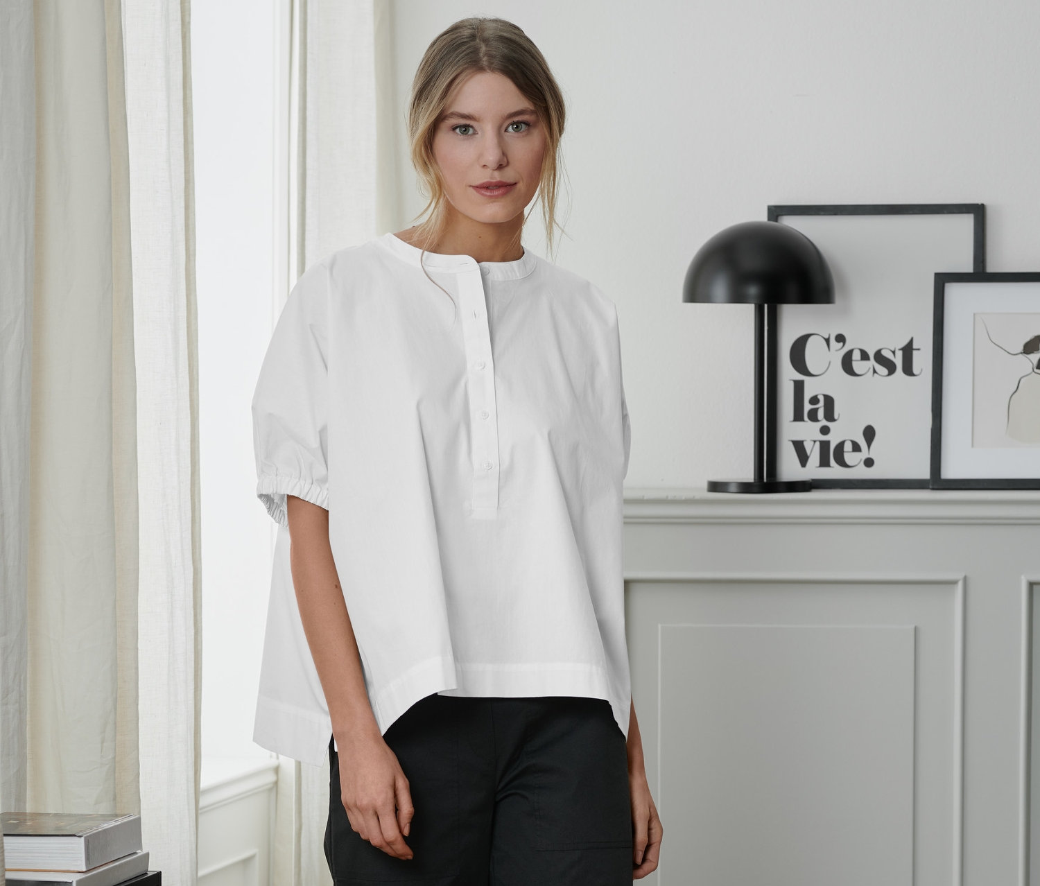 Frau steht in weißer Popeline-Bluse und schwarzer Hose.