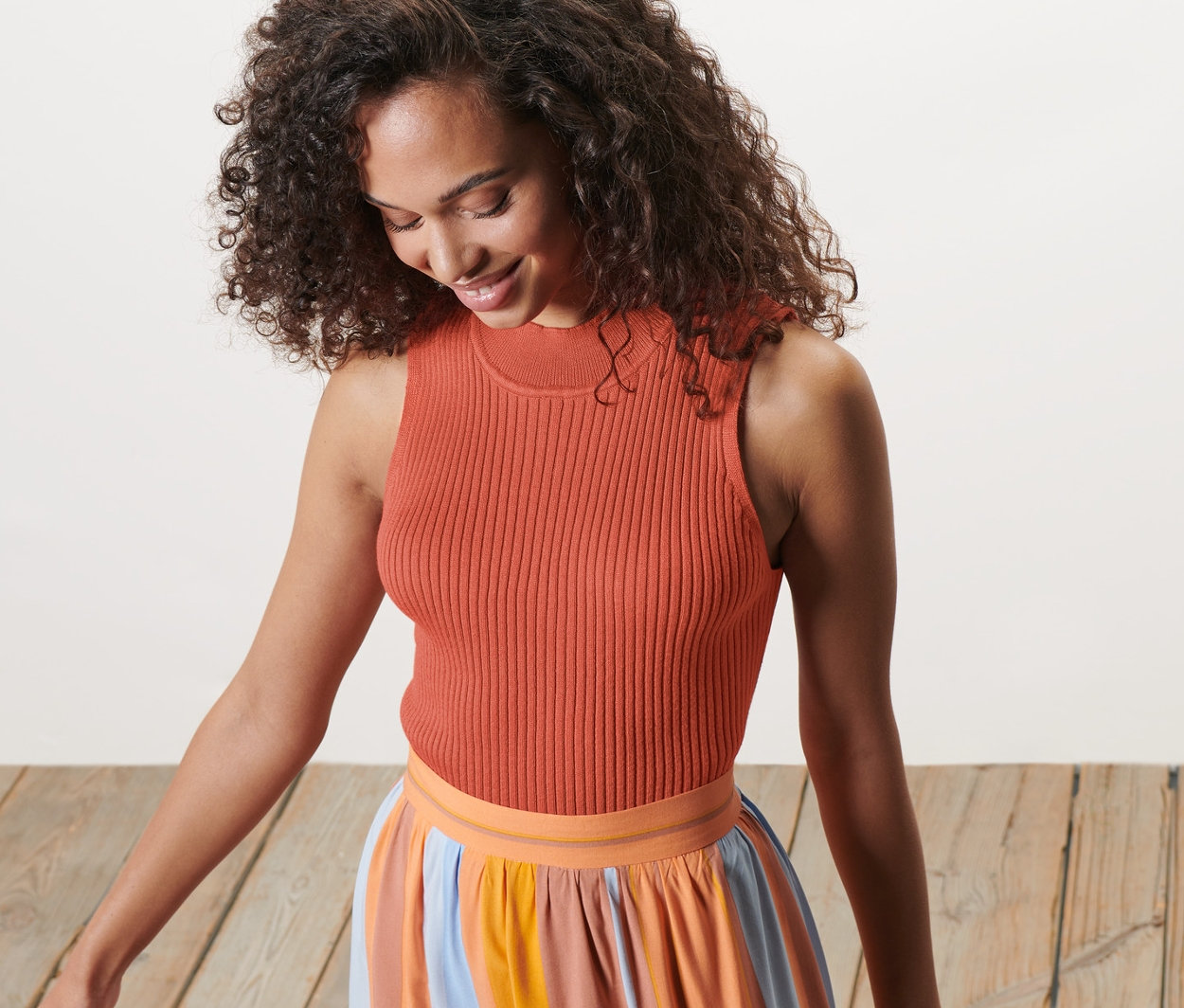 Frau mit Stricktop und gestreiftem Rock schaut nach unten.