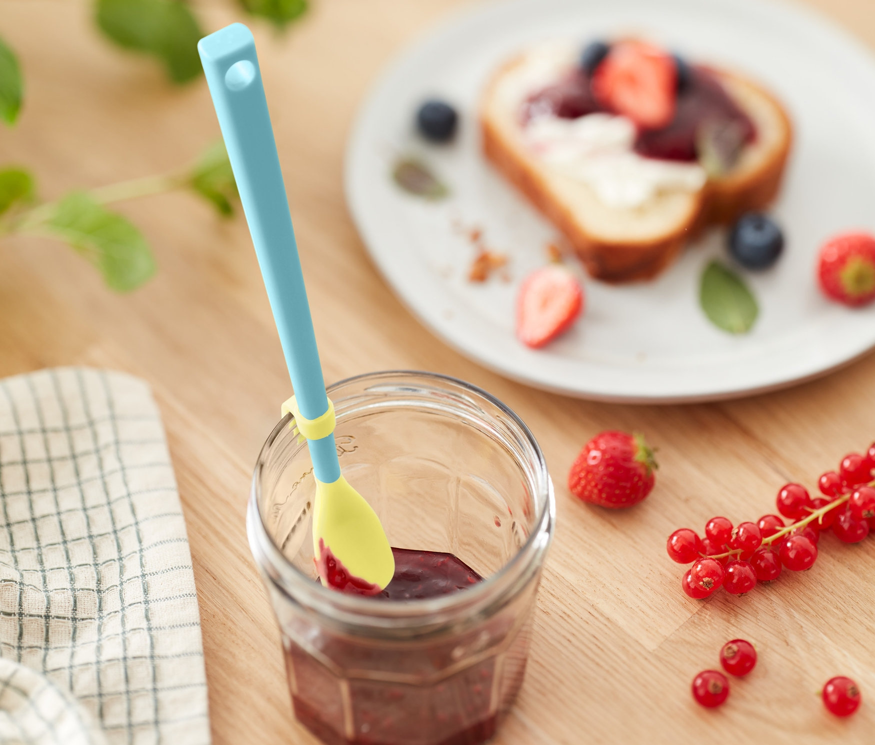 Ein Marmeladenglas mit Spezial-Silikonlöffel, daneben ein Brot mit Früchten.