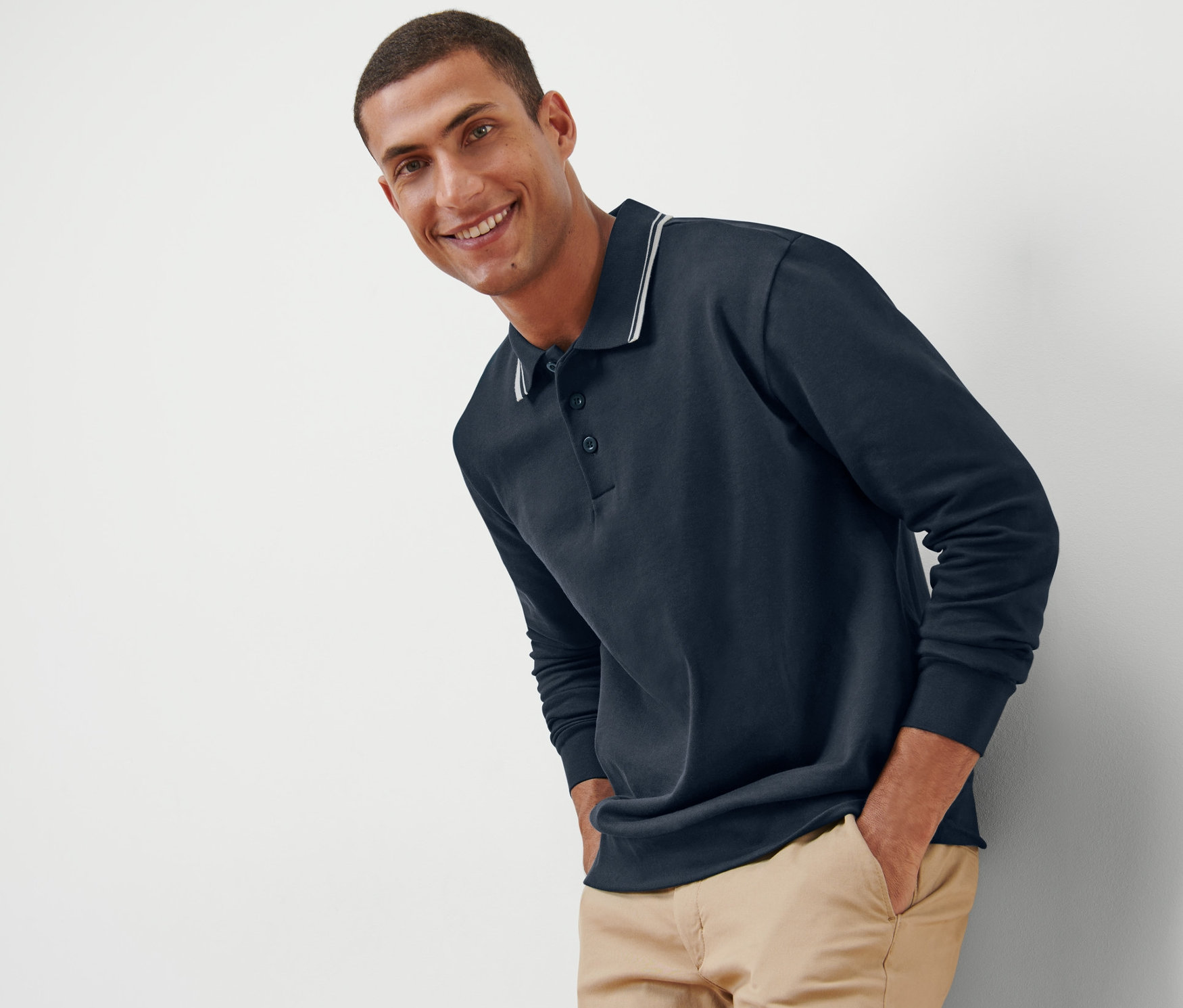 Ein lächelnder Mann posiert in einem Sweatshirt mit Polokragen und beigen Hosen.