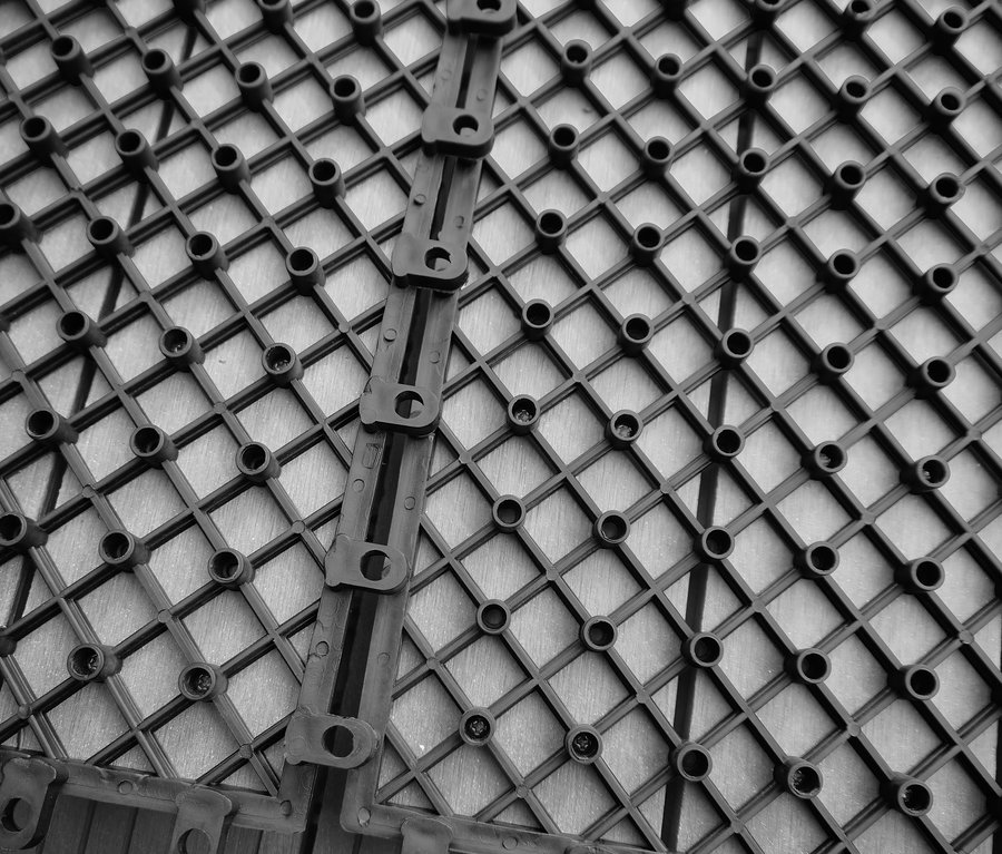 Detailaufnahme von hellgrauen 30 x 30 cm WPC Terrassenfliesen mit Gittermuster.