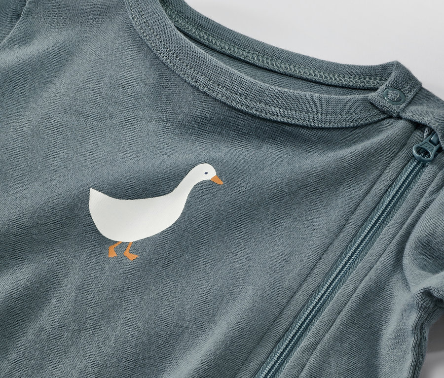 Detailaufnahme eines blauen Baby-Pyjamas mit einer Gans-Applikation und Reißverschluss.