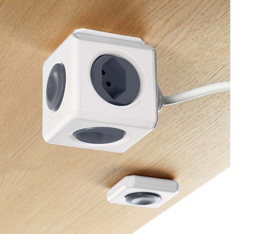 Auf einer Holzoberfläche befindet sich ein weißer Steckdosenwürfel mit Fernbedienung.