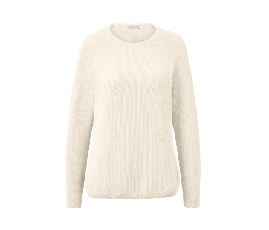 Frau sitzt auf Holzboden und trägt einen cremeweißen Strickpullover.