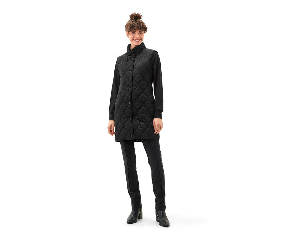 Frau trägt eine schwarze Parka mit Weste, schwarze Hose und Stiefel.