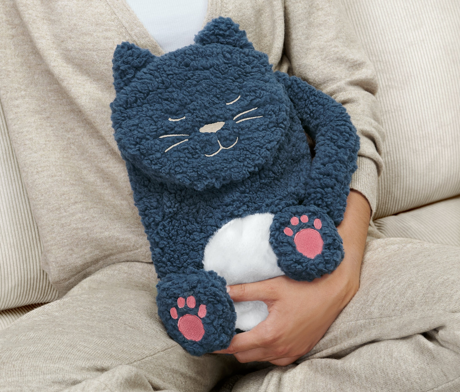 Frau sitzt auf Couch und hält Wärmflasche »Katze«.