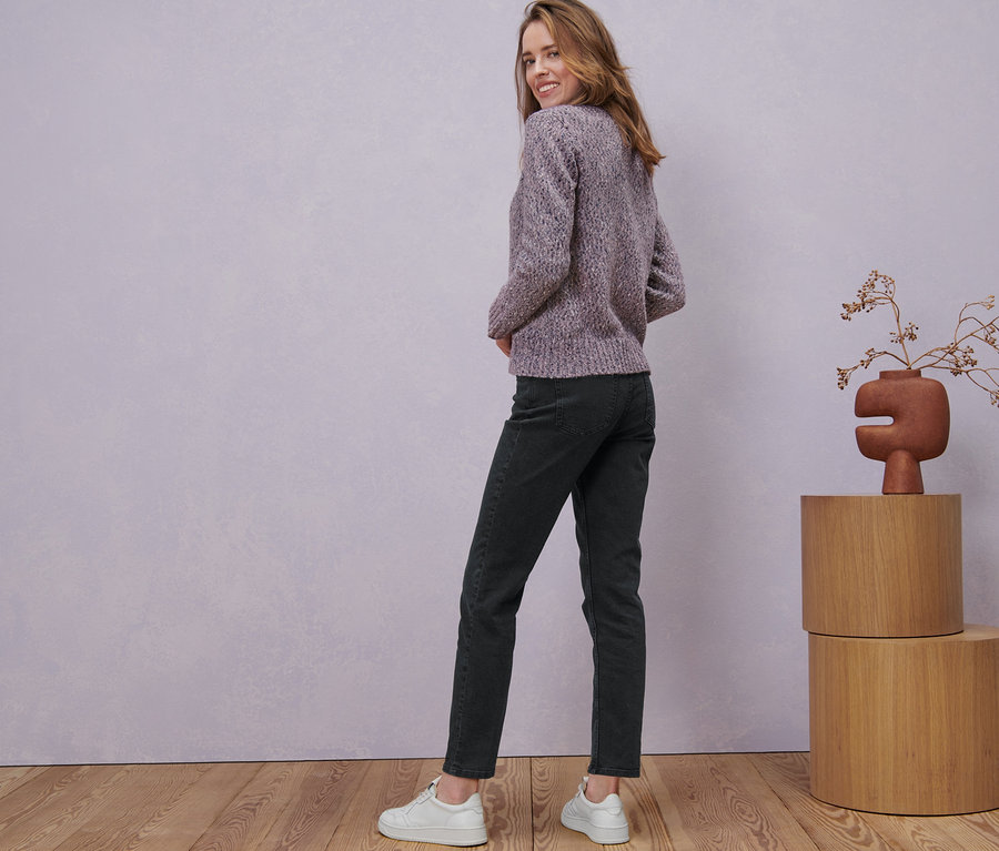 Frau blickt über die Schulter und posiert in Strickjacke mit Wolle, Jeans und Turnschuhen.