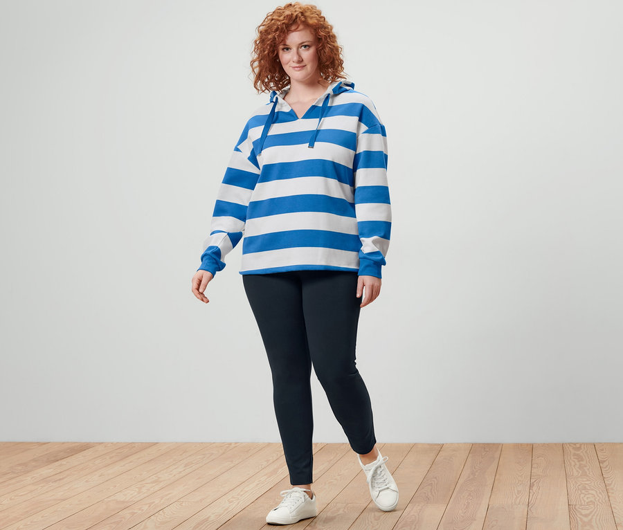 Rothaarige Frau posiert in gestreiftem Hoodie und schwarzen Heavy-Leggings.