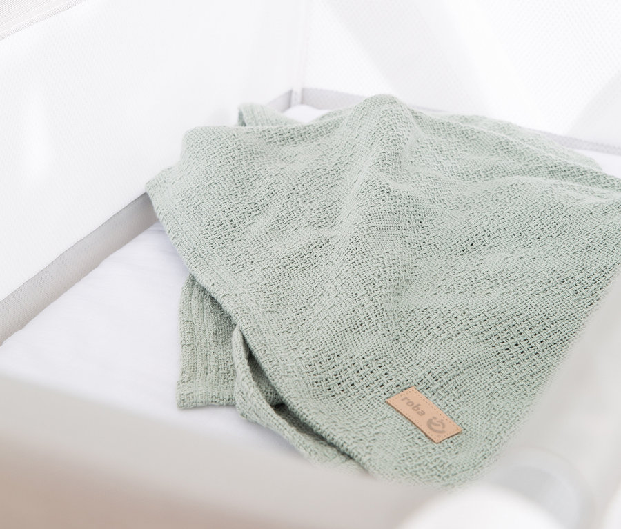 Eine grüne Decke liegt in einem weißen, klappbaren Stubenbett von roba.